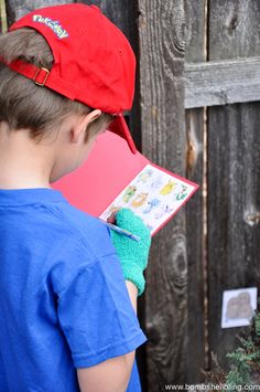 a young boy wearing a red hat and blue shirt holding an open book in front of a wooden fence