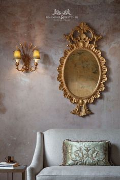 An ornate mirror in a gold finish hanging above a small, traditionally crafted sofa. Gold Wall Lights, British Furniture, Ornament Drawing, Statement Chandeliers