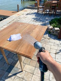 a person using a power drill to paint a wooden table on the side of a lake