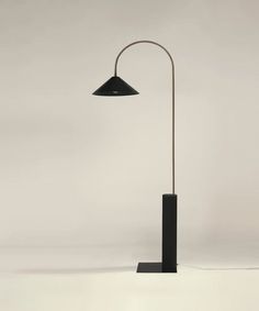 a floor lamp with a black shade on the base and a white wall behind it