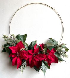 a christmas wreath with poinsettis and greenery hanging from the side on a white wall