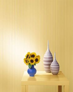 two vases with sunflowers sit on a small table in front of a striped wall