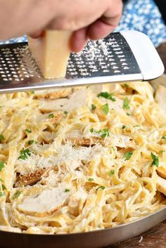 someone grating cheese on top of pasta in a pan