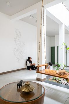 a woman sitting on a swing in the middle of a room with white walls and wood flooring