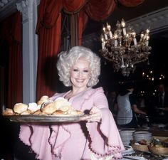 a woman holding a tray with pastries on it in front of a chandelier