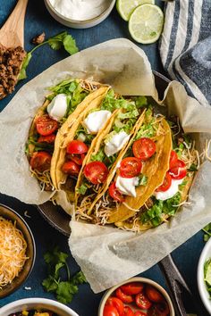 three tacos with tomatoes, lettuce and sour cream on top in bowls