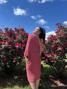 a woman is standing in front of some bushes and flowers wearing a pink sweater dress