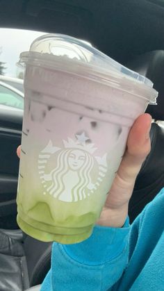 a person holding up a starbucks drink in their hand while sitting in the back seat of a car