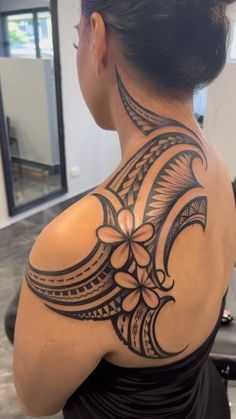 the back of a woman's neck with an intricate tattoo design on her left shoulder