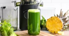 a green smoothie sitting on top of a wooden cutting board next to other fruits and vegetables