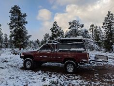 a red pick up truck parked on top of a snow covered field with trees in the background