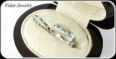 two white gold wedding bands with blue topaz and green diamonds in a ring box