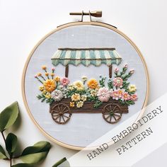 an embroidery pattern with flowers in a wagon and awning on the side, surrounded by greenery