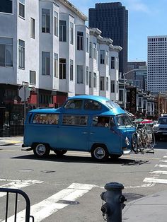 a blue van driving down a street next to tall buildings