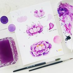 some purple flowers are sitting on a table next to watercolor paints and a brush