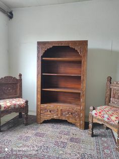 two wooden chairs and a bookcase in a room with rugs on the floor