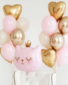 a cat balloon sitting on top of a white vase filled with pink and gold balloons