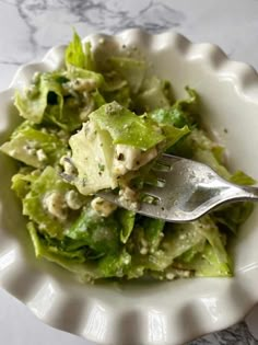 a white bowl filled with lettuce on top of a marble counter next to a fork