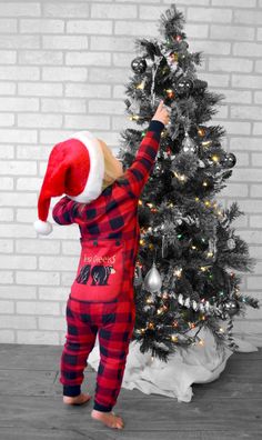 a little boy wearing a santa hat next to a christmas tree in front of a brick wall