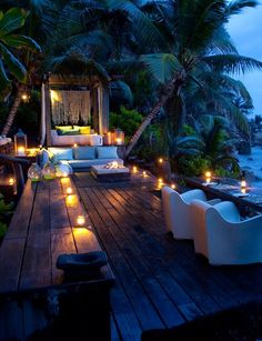 an outdoor seating area with candles lit on the ground and palm trees in the background