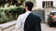 a man with a beard and glasses is walking down the street in front of a car