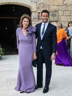 a man and woman standing next to each other in front of a stone building with people walking around