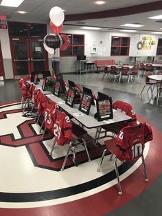 a large room with tables and chairs covered in red cloths, balloons and pictures hanging from the ceiling