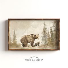 a bear and her cub are standing in the woods, framed on a white wall