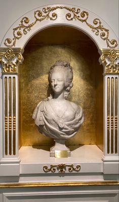 the bust of a woman is on display in front of a gold and white wall