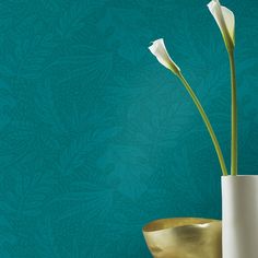 two white flowers in a gold vase against a teal wallpapered background,