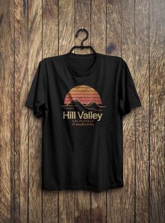 a black t - shirt hanging on a wooden wall with the words hill valley written across it