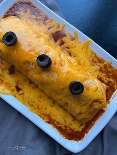 an enchilada covered in cheese and black olives on a white plate