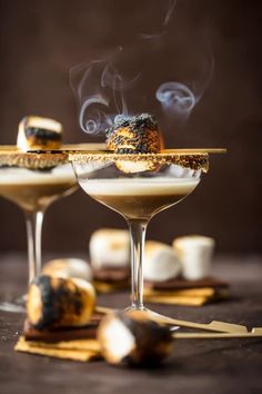 two martini glasses filled with ice cream and topped with marshmallows, cinnamon sticks, and whipped cream