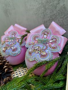 two pink christmas baubles sitting next to pine cones and fir branches with bows on them