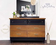 a dresser with two drawers and a clock on top, in front of a white wall