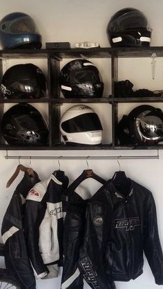 several motorcycle helmets and jackets are hanging on a rack in a room with other items