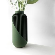 a green vase with flowers in it on a white surface, against a plain background