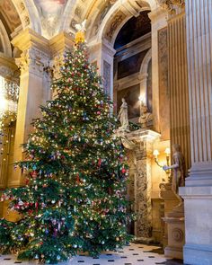 a large christmas tree in the middle of a room with marble floors and walls, decorated with gold trimmings