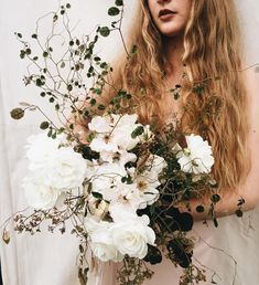 a woman with long hair holding a bouquet of white flowers and greenery in her hands