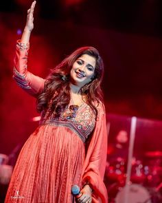 a woman in an orange dress on stage with her hand up to the sky and holding a microphone