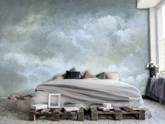 a large bed sitting in the middle of a bedroom next to a wall with clouds painted on it