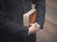 a man in a black suit holding a book and wearing a white glove on his left hand