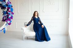 a woman in a blue dress sitting on a white chair next to a floral wreath