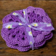 purple crocheted coasters with white daisies on them sitting on a wooden surface