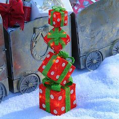 a small christmas tree made out of presents in the snow next to other holiday gifts