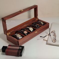 Elegantly showcase and protect your timepieces with this handcrafted wooden watch box featuring a sleek glass lid. Designed with five individual slots, this watch case is perfect for organizing and displaying your watches in style. The soft velvet-lined compartments cradle each timepiece, preventing scratches and damage, while the clear glass lid allows for easy viewing without opening the box. Crafted from premium wood with brass hinges and a secure clasp, this watch box is not only functional Wooden Watch Box, Watch Safes, Watch Storage Box, Handmade Watch, Watch Storage, Brass Hinges, Watch Display, Wooden Watch, Perfect Gift For Him