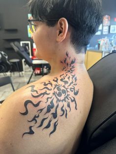 the back of a woman's neck is covered with black ink and has a sun tattoo on it