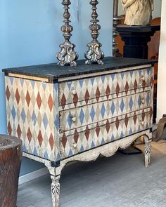 an old dresser with two candles on top and a statue in the back ground next to it