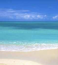 an empty beach with blue water and white clouds in the sky, on a sunny day