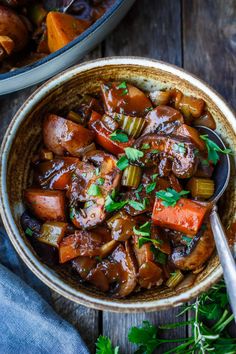 a bowl filled with stew and carrots on top of a wooden table